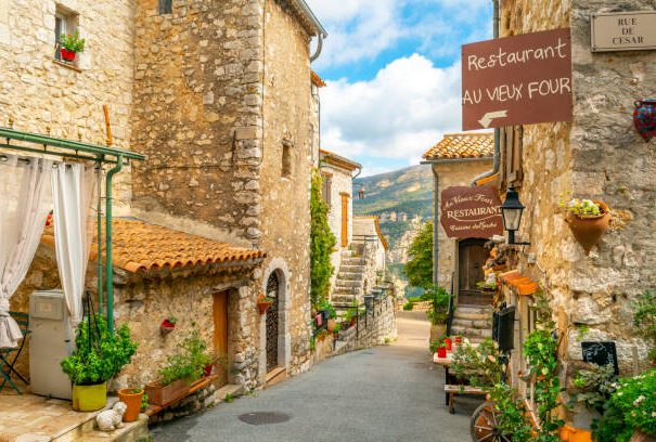 Explorez une charmante rue pavée ornée de fleurs colorées dans le village perché de Gourdon, l'un des plus beaux villages de France. Cette scène typique illustre le charme provençal et l'authenticité de ce village médiéval offrant une vue panoramique sur la Côte d'Azur.